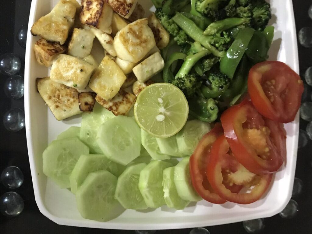 Grilled paneer with broccoli, cucumber and tomato on a plate, a low-carb evening meal