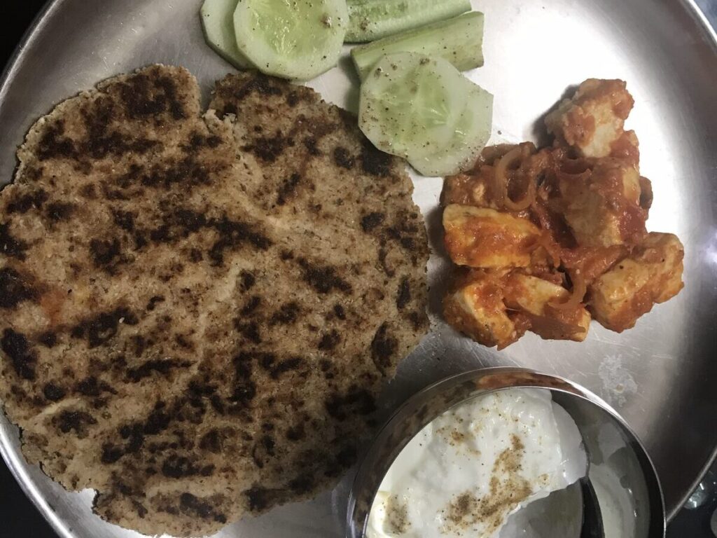 Keto roti with paneer tikka masala, curd and cucumber salad on a steel thali
