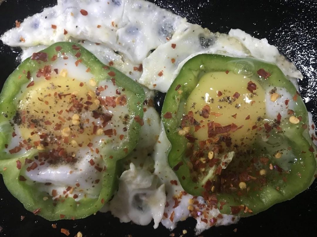 Two capsicum egg rings in a pan, dusted with red chilli flakes