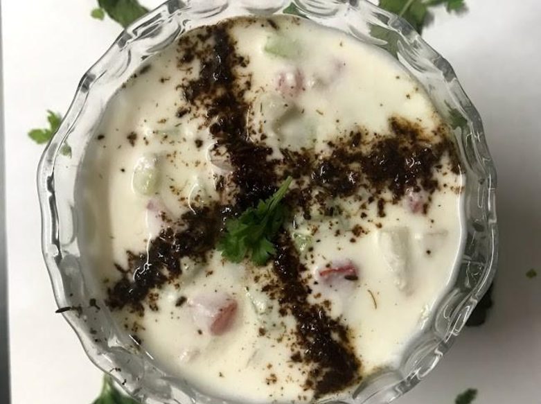 Cucumber onion tomato raita in a glass bowl, dusted with roasted cumin