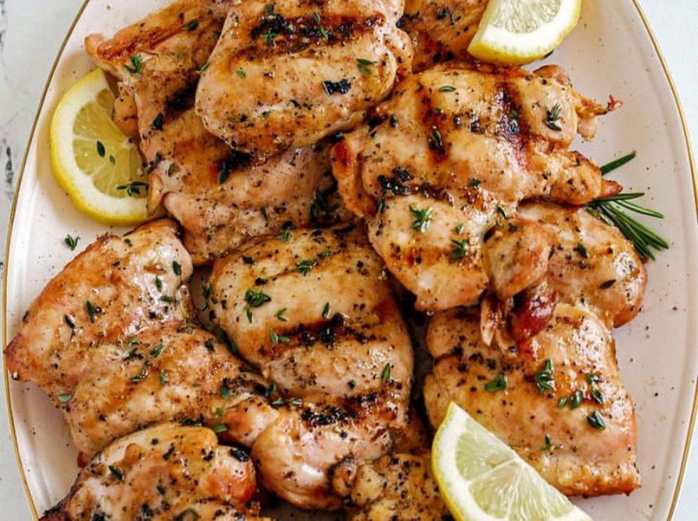 Grilled chicken pieces with lemon wedges and dried herbs on a plate