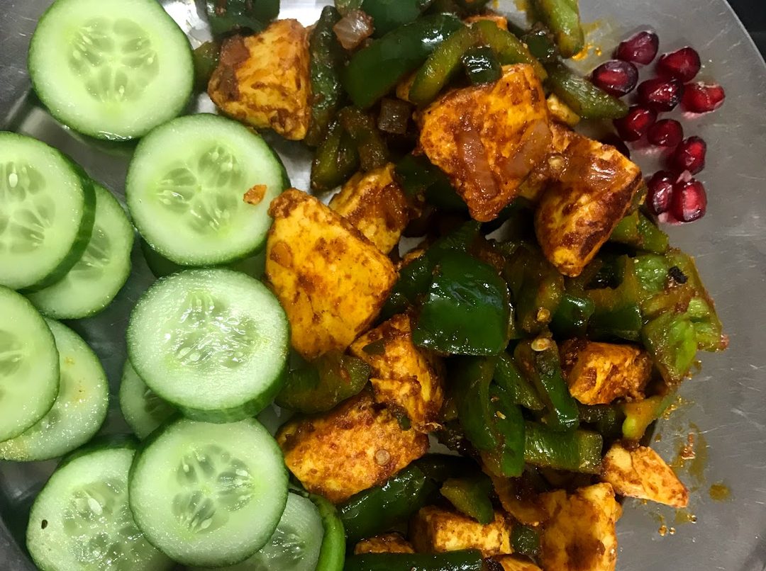 Paneer tikka plated with cucumber, sliced onion and pomegranate seeds